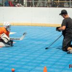 Coach montre à un jeune gardien de dek hockey comment bien se positionner pour le papillon